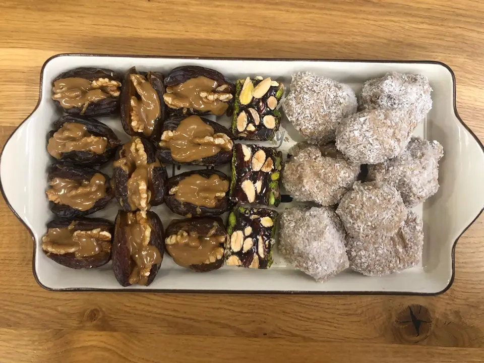 A homemade platter of walnut-stuffed dates beside date and coconut sweets